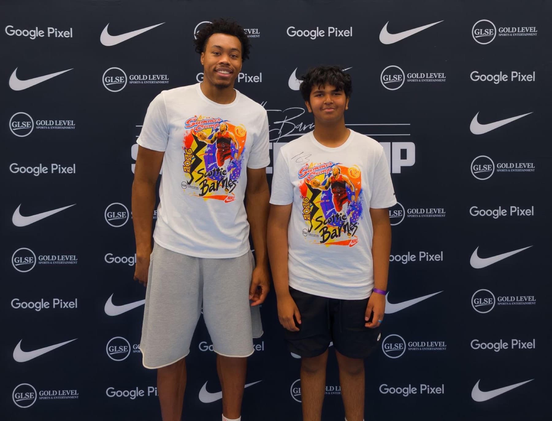 Mir Kahol standing beside Toronto Raptors player Scottie Barnes at a summer camp media backdrop