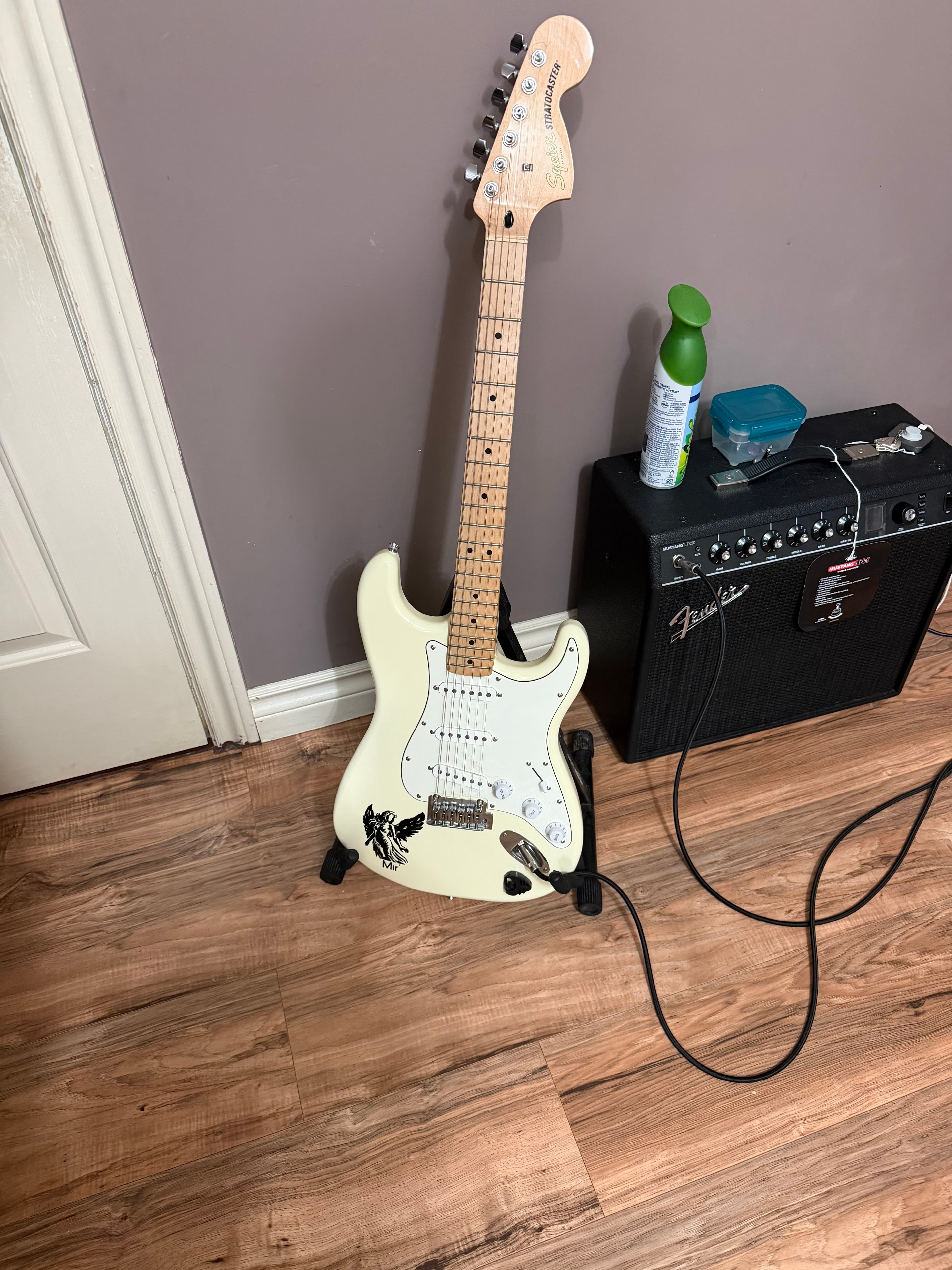 White Squier Stratocaster electric guitar with a custom Mir eagle decal, resting on a stand