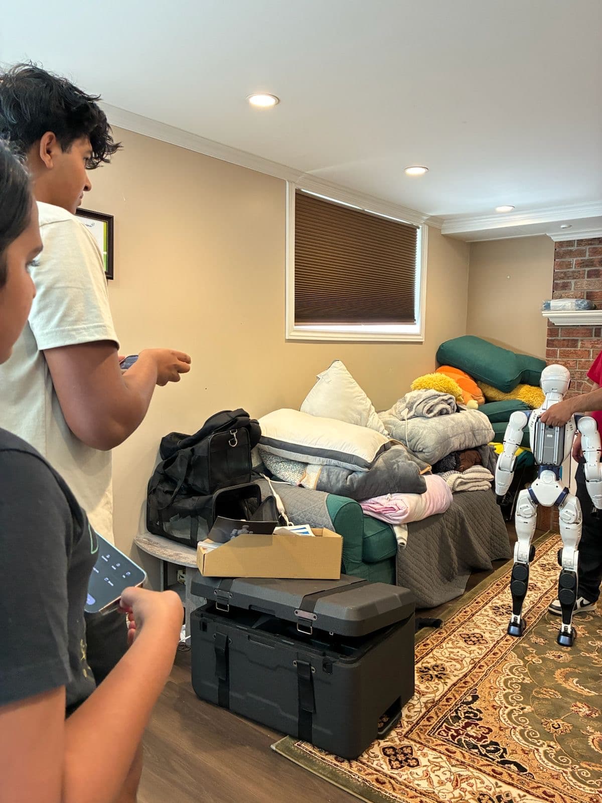 A white humanoid robot standing and walking on a rug while two people control it from their phones