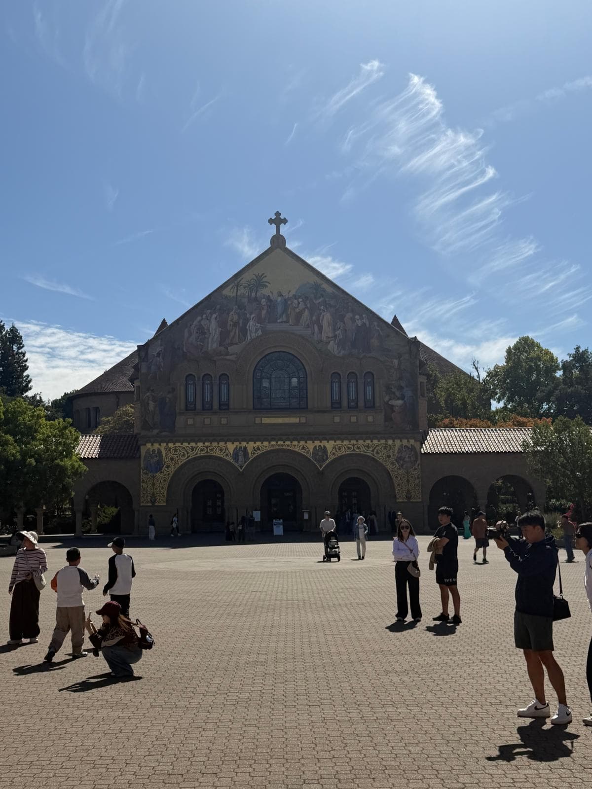 Stanford Memorial Church with its gold mosaic facade under a blue sky, with visitors in the Main Quad